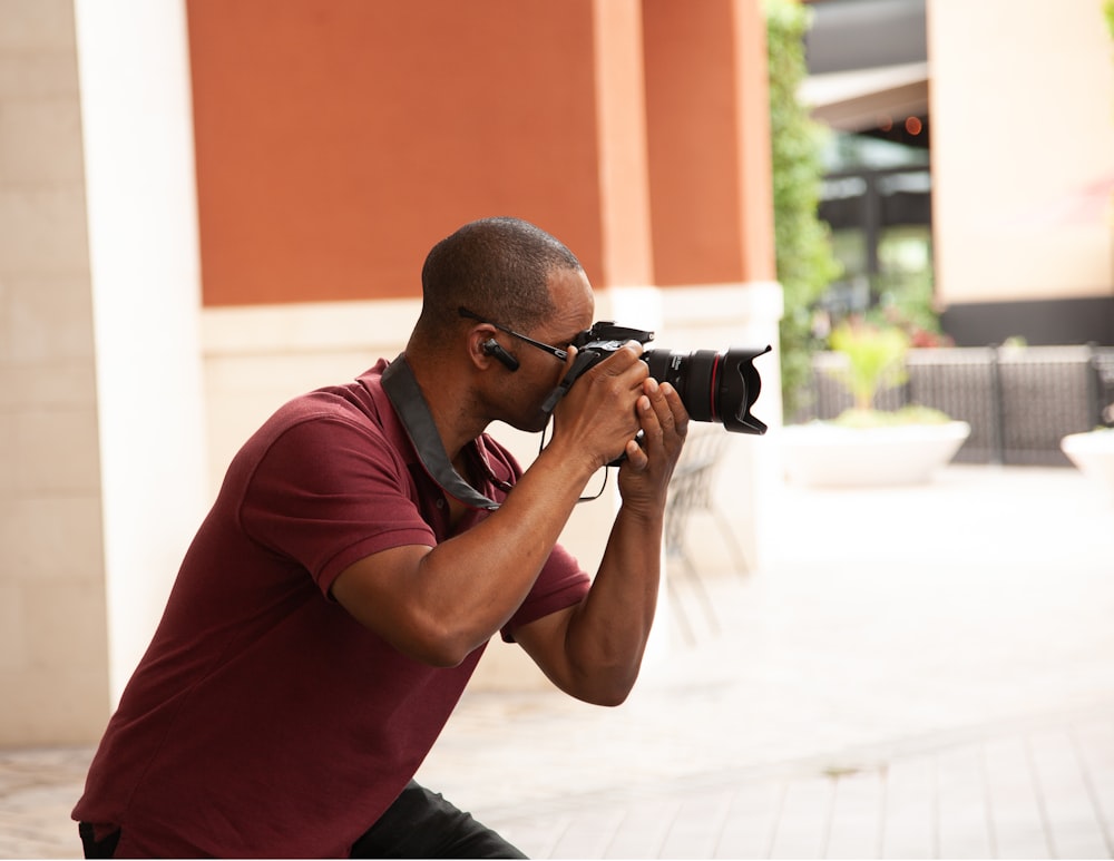man in maroon polo shirt holding black dslr camera