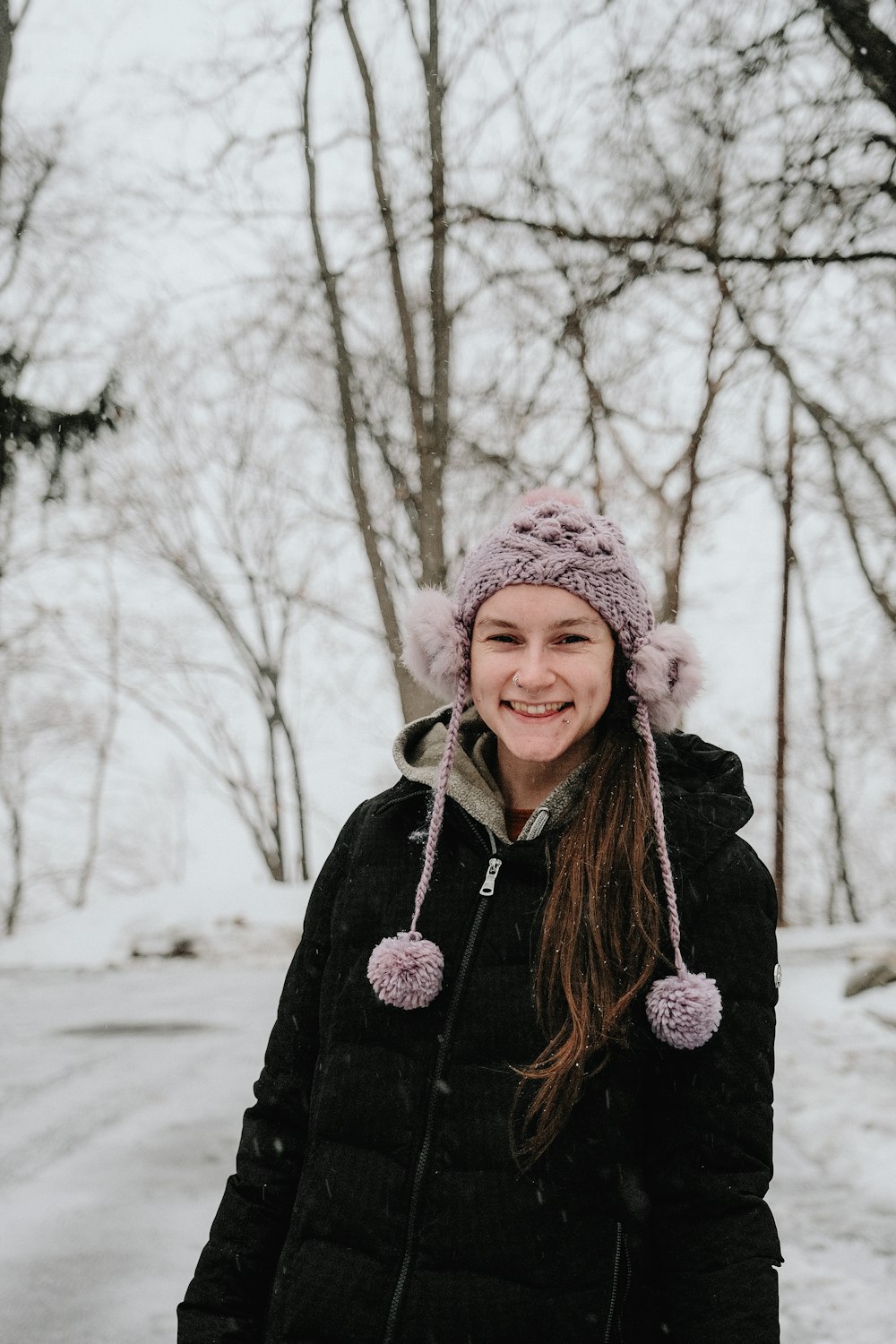 woman in black coat wearing white knit cap standing near bare trees during daytime