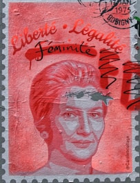 A stylized portrait of a woman is depicted on a textured surface resembling a stamp. The image is dominated by shades of red and pink. Written text in stylized fonts includes the words 'Liberté', 'Légalité', and 'Féminité'. The top right corner features a postmark stamp with the year 1975 and the location Bobigny. Black scribbles overlay parts of the image.