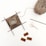 A small piece of knitting is in progress with four knitting needles positioned around it, accompanied by a ball of yarn. Nearby are a pair of ornate scissors and three small labels with sewing and knitting motifs.