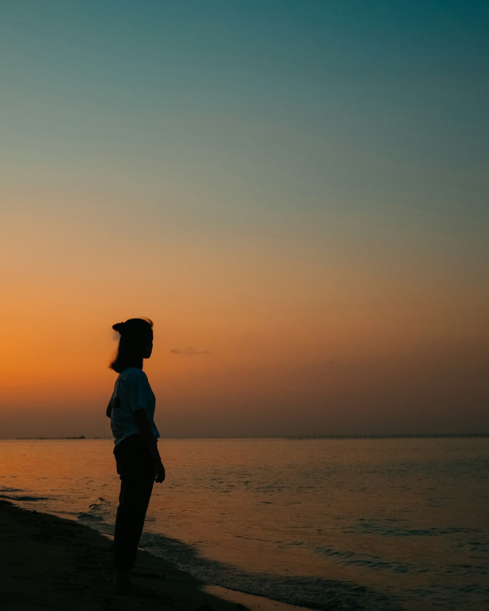 silhouette of woman standing on beach during sunset