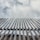 A series of vertical bamboo poles are aligned in a row, reaching towards a cloudy sky. The bamboo appears weathered and is tied together at intervals. The image has a strong upward perspective.