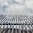 A series of vertical bamboo poles are aligned in a row, reaching towards a cloudy sky. The bamboo appears weathered and is tied together at intervals. The image has a strong upward perspective.