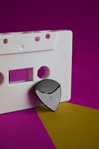 A sleek cassette tape glowing with neon pink light against a dark cosmic background sprinkled with cherry blossom petals.