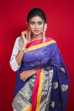 A graceful model draped in a maroon designer saree standing against a soft pastel background.