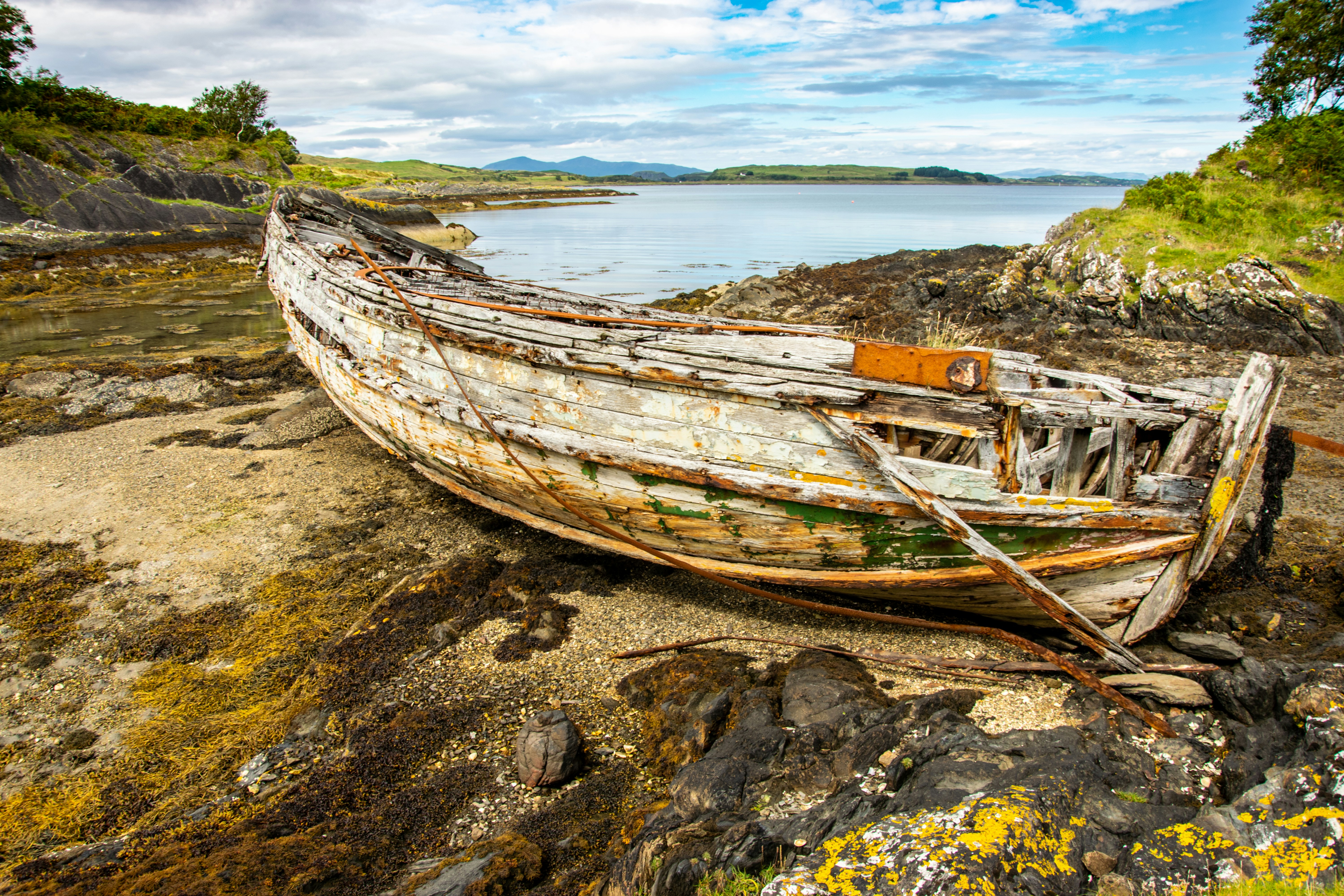 brown wooden boat on shore during daytime, The old Isle of Luing ferry abandoned on a remote beach not far from the Isle of Luing on the west coast of Scotland. 