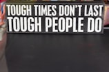A rectangular sign displays the motivational phrase 'Tough times don't last, tough people do' in bold, white capital letters on a black background.