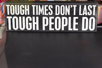 A rectangular sign displays the motivational phrase 'Tough times don't last, tough people do' in bold, white capital letters on a black background.