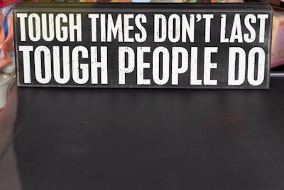 A rectangular sign displays the motivational phrase 'Tough times don't last, tough people do' in bold, white capital letters on a black background.