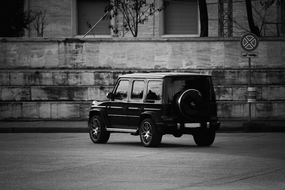 grayscale photo of suv parked beside wall