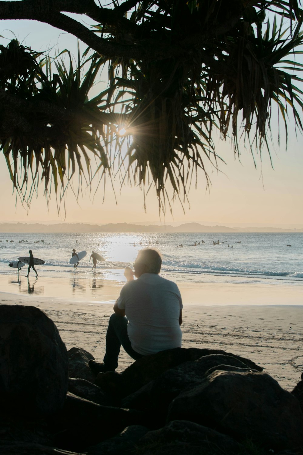 man in white shirt sitting on beach shore during sunset