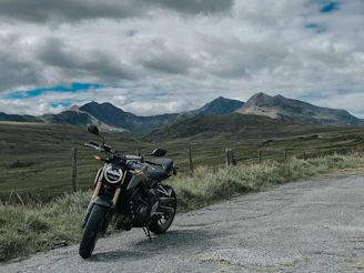 black motorcycle parked on gray asphalt road near green grass field and mountain under white clouds