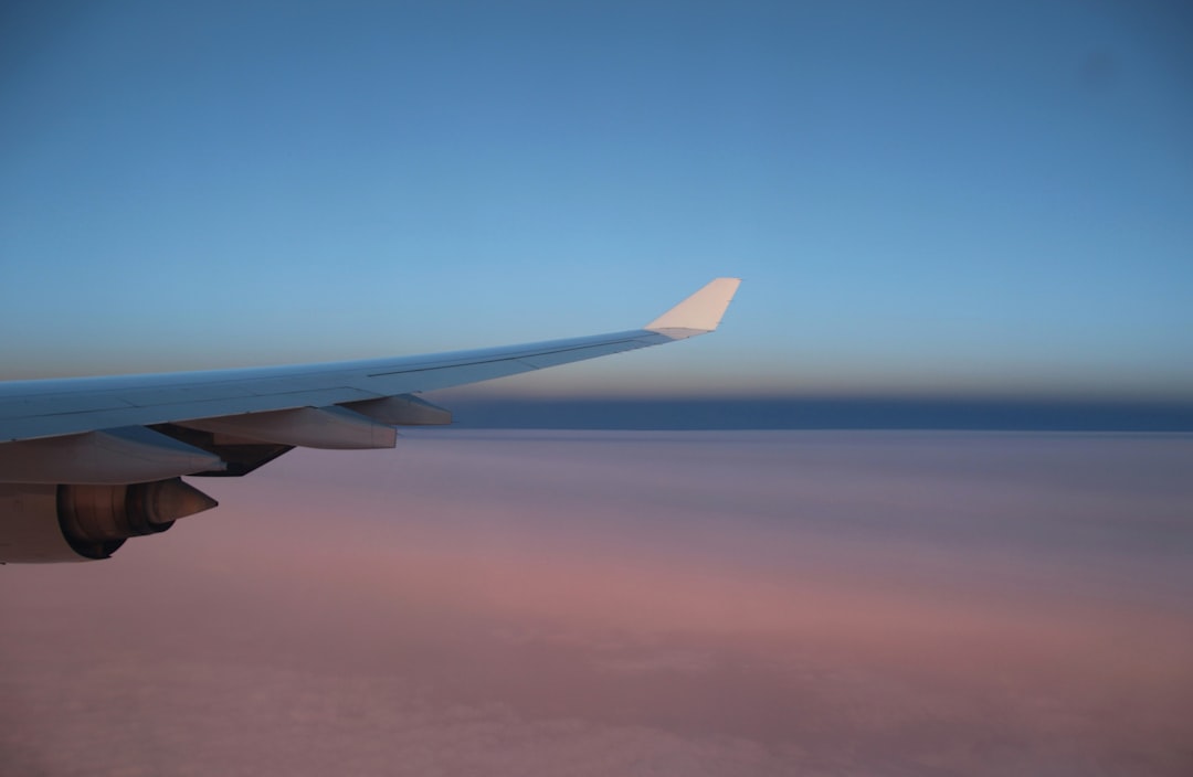 white airplane wing over blue sky during daytime, On an evening flight over the Sahara desert. Wing of the airplane and beautiful desert landscape in pink colors far below. Africa.