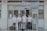 Four individuals stand in front of a building wearing formal button-down shirts with name tags. They are positioned near a sign above the door with details in Vietnamese. The setting appears academic or professional, likely related to a university or educational institution.
