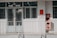 A building entrance with metal barred doors and windows, featuring signs indicating it belongs to a faculty for high-quality training. The facade is white, and there are red fire extinguishers and safety notices mounted on the wall next to the entrance.