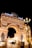 An elaborate architectural structure featuring an archway adorned with sculptures and intricate carvings. The entrance is illuminated with bright lights, and figures of horses and a chariot are positioned on top. The word 'Europe' is displayed in bold, bright lettering. Many people are gathered around the entrance under the night sky.