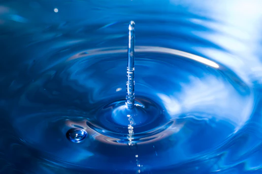 A serene water droplet splashing onto a clear, blue surface under bright sunlight.