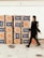 A person wearing a mask walks past a stack of cardboard boxes labeled 'Love Box' and adorned with Home Depot logos. The boxes are neatly organized against a light-colored wall.