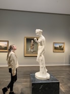woman in beige coat standing near white statue