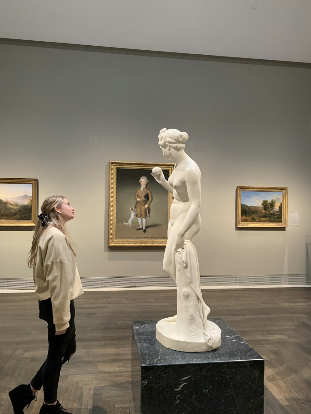 woman in beige coat standing near white statue