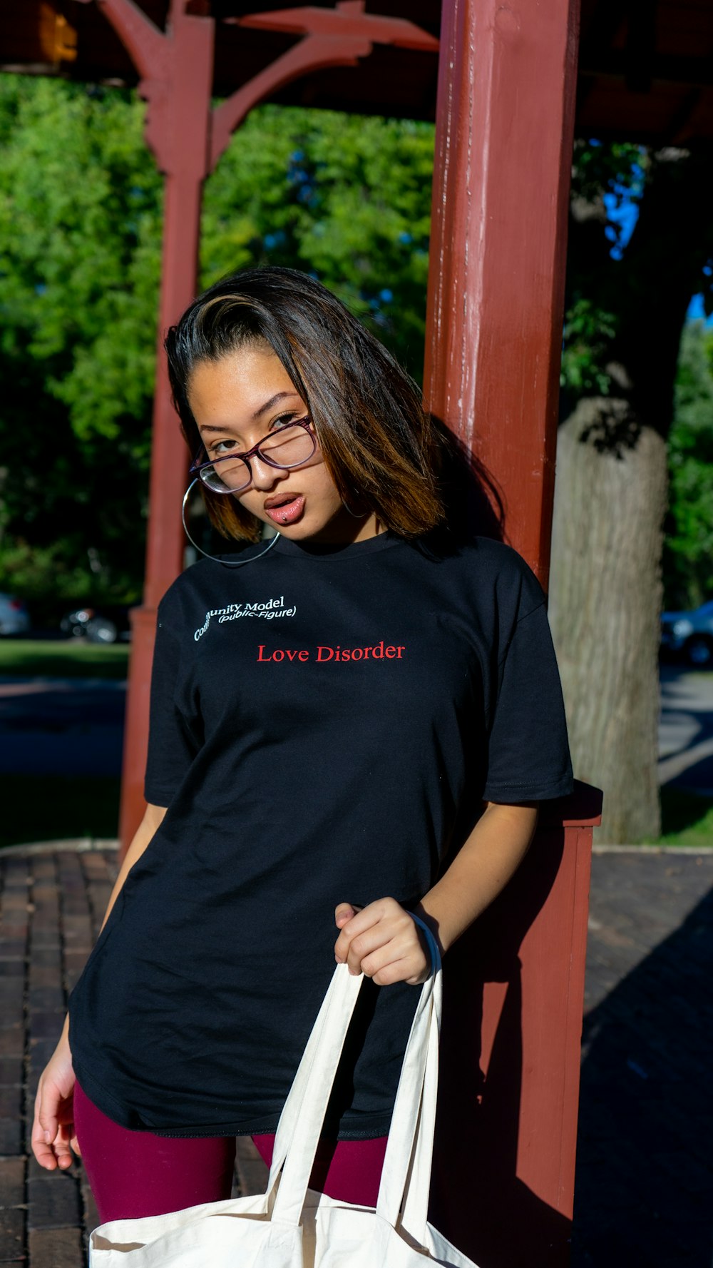 mulher na camiseta preta do pescoço da tripulação e óculos de sol pretos em pé perto do poste de madeira vermelho durante