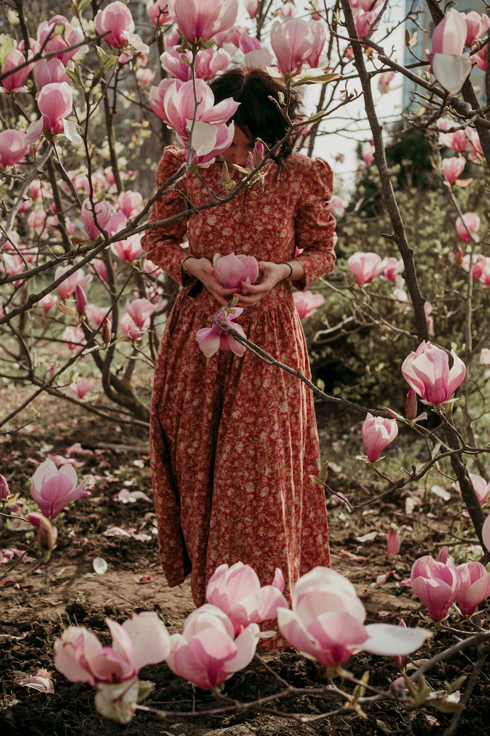 빨간 드레스를 입은 여자가 분홍색 꽃 근처에 서 있습니다.