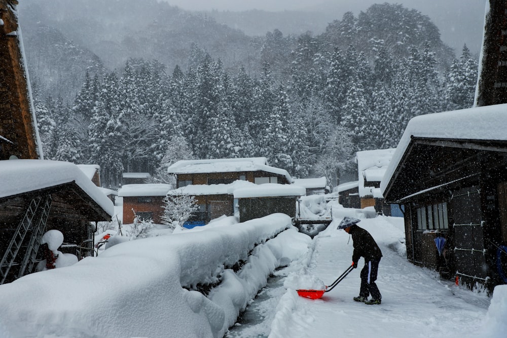 person in black jacket and blue pants holding snow shovel on snow covered ground during daytime