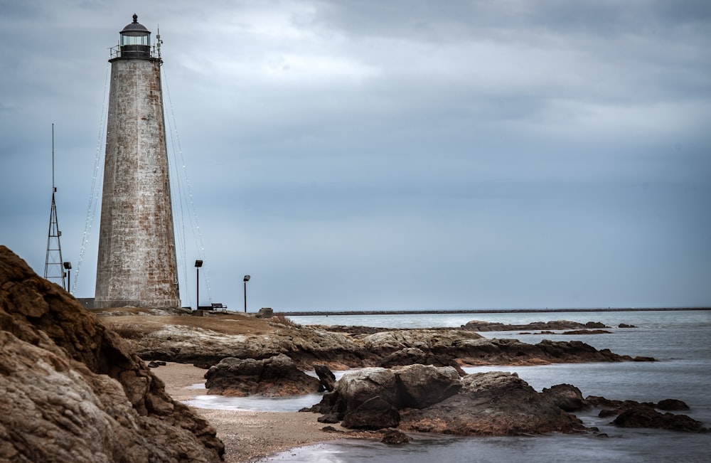 white and black lighthouse on brown rocky shore under blue sky during daytime