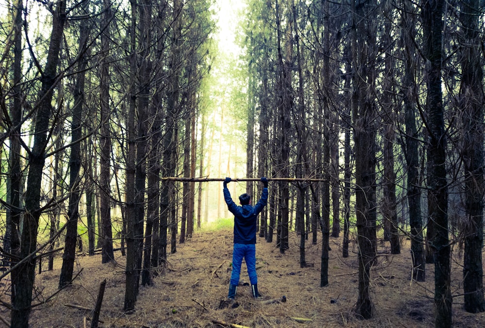 man in blue jacket standing on brown field surrounded by trees during daytime