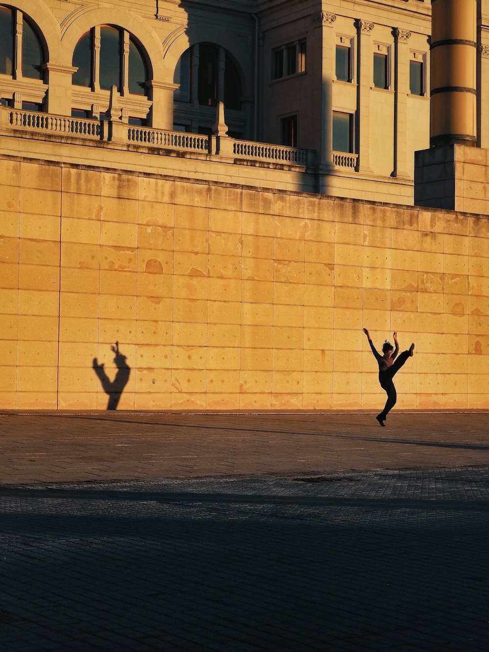 man in black jacket and pants jumping near beige concrete building during daytime