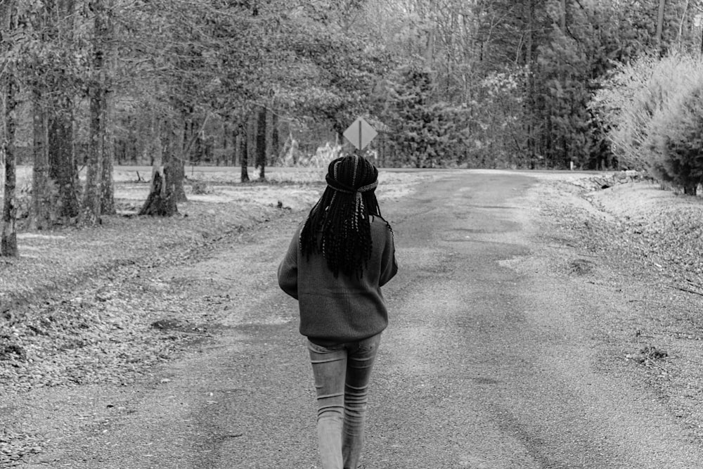 woman in black jacket and blue denim jeans walking on road in grayscale photography