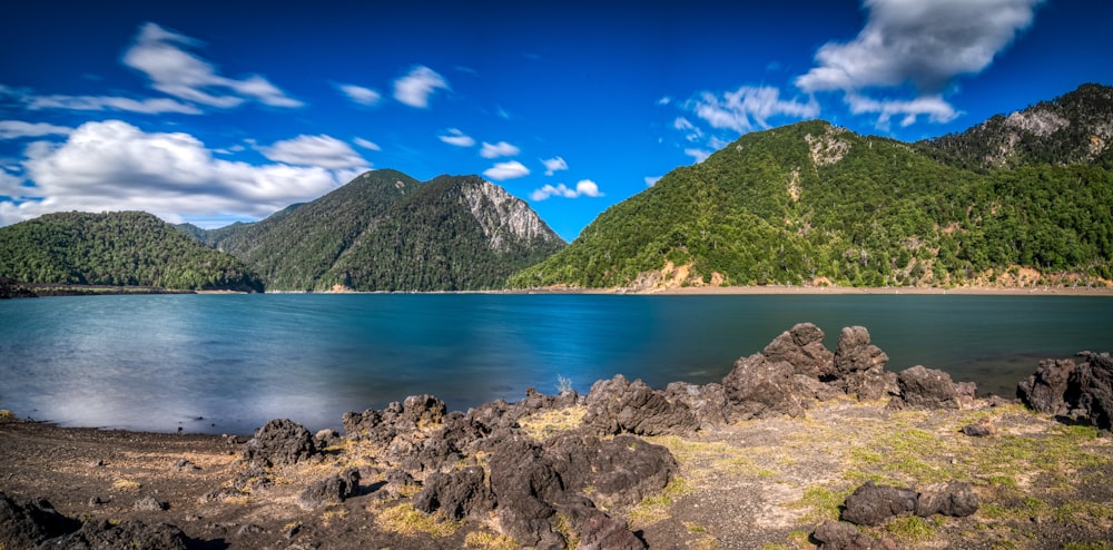 日中の青空の下、水域近くの茶色の岩層