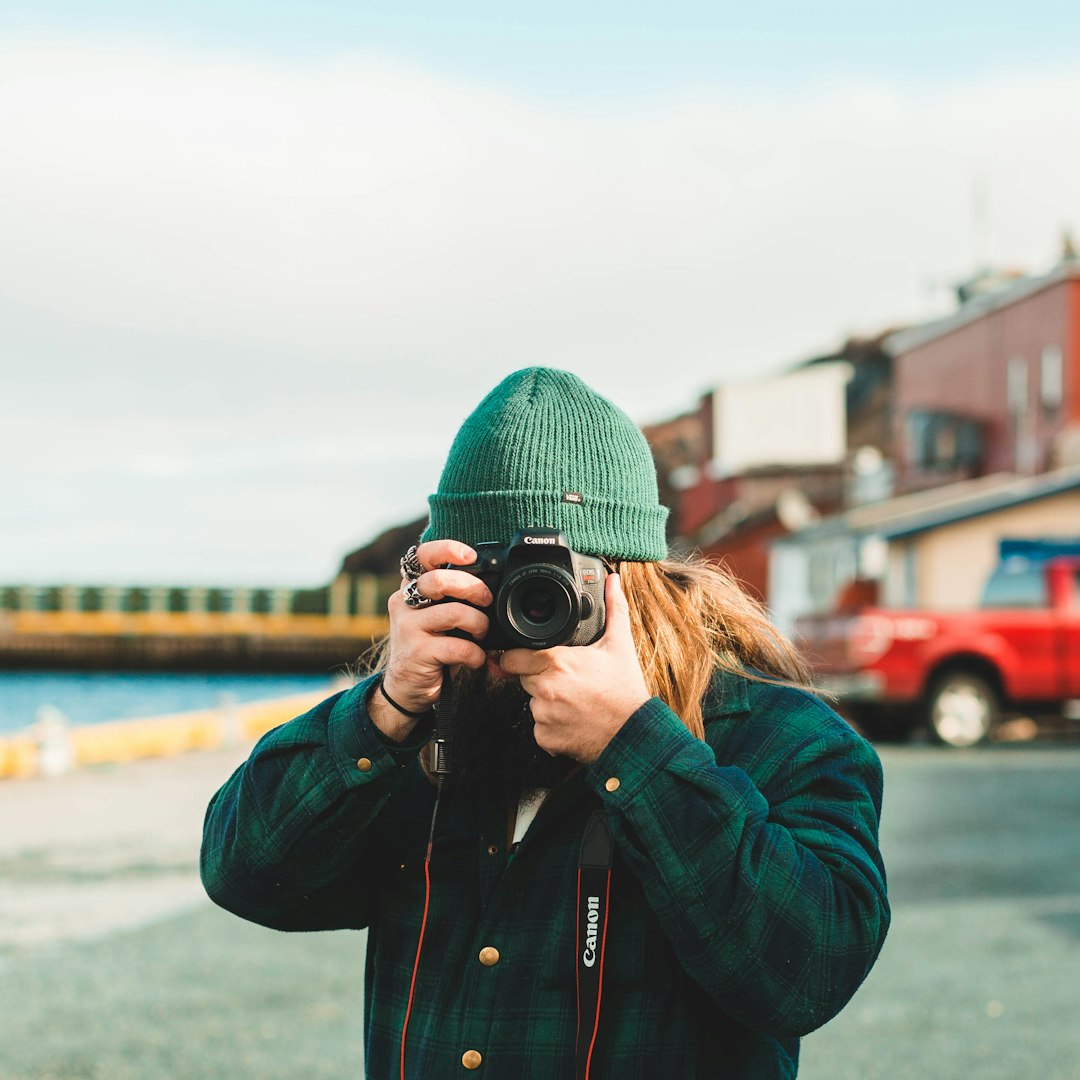 woman in green knit cap and black jacket taking photo using black dslr camera