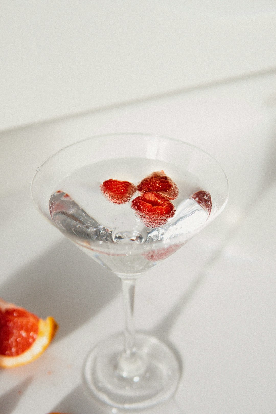 martini glass with clear liquid and raspberries.  