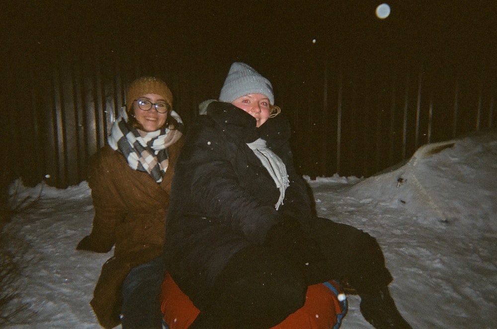 man and woman sitting on snow covered ground during night time