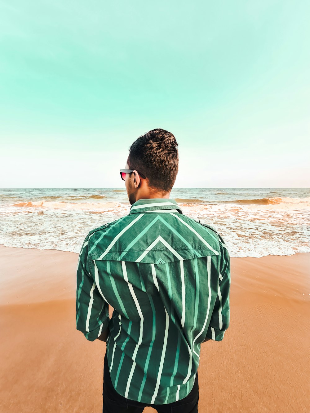 man in green and white stripe shirt standing on beach during daytime