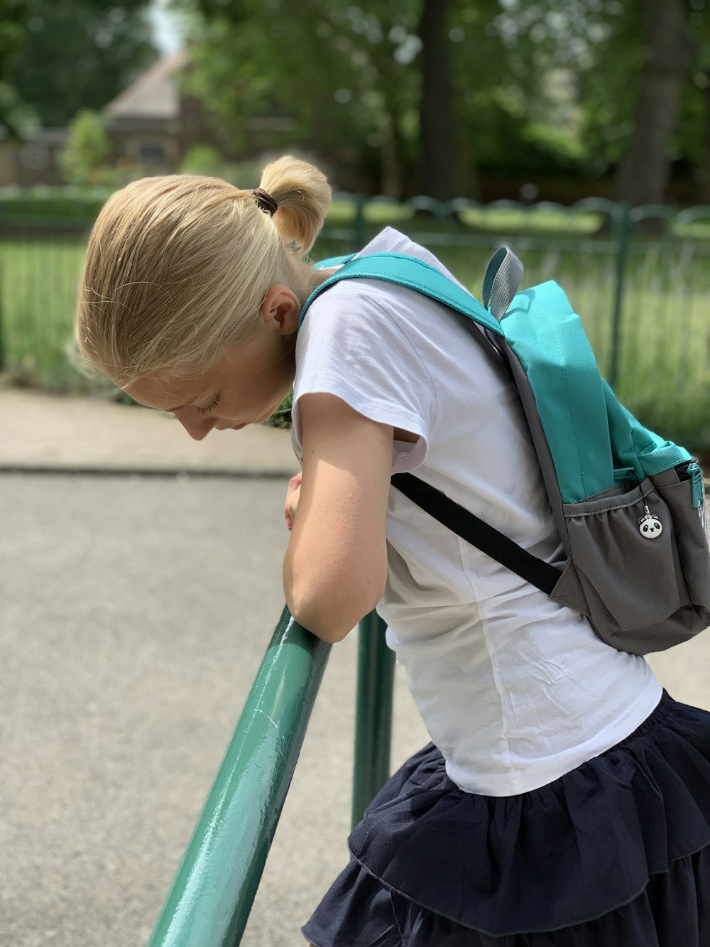 boy in white t-shirt and blue backpack standing on green metal railings during daytime