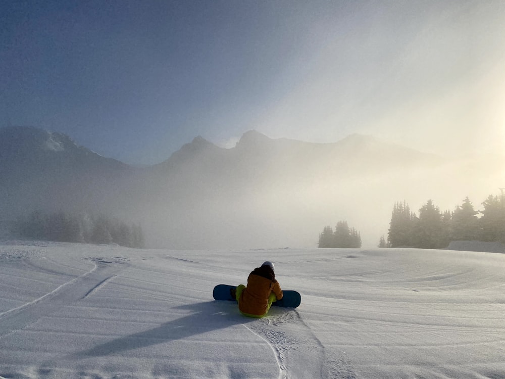 person in yellow jacket sitting on snow covered ground during daytime