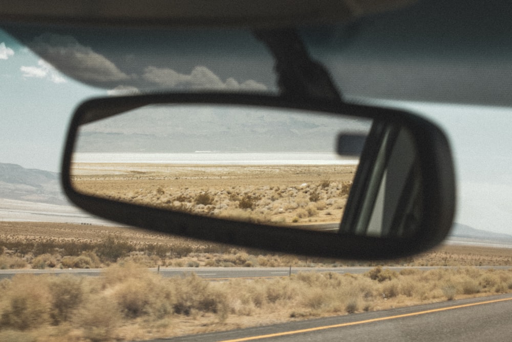specchietto laterale nero dell'auto che riflette il campo marrone durante il giorno