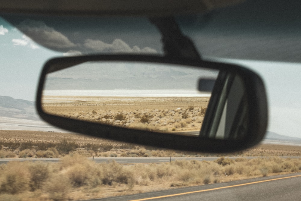 black car side mirror reflecting brown field during daytime