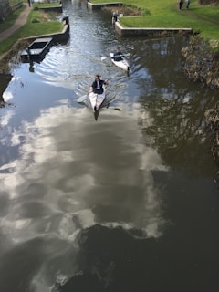 Two kayakers gliding side by side through a narrow river surrounded by lush green trees.