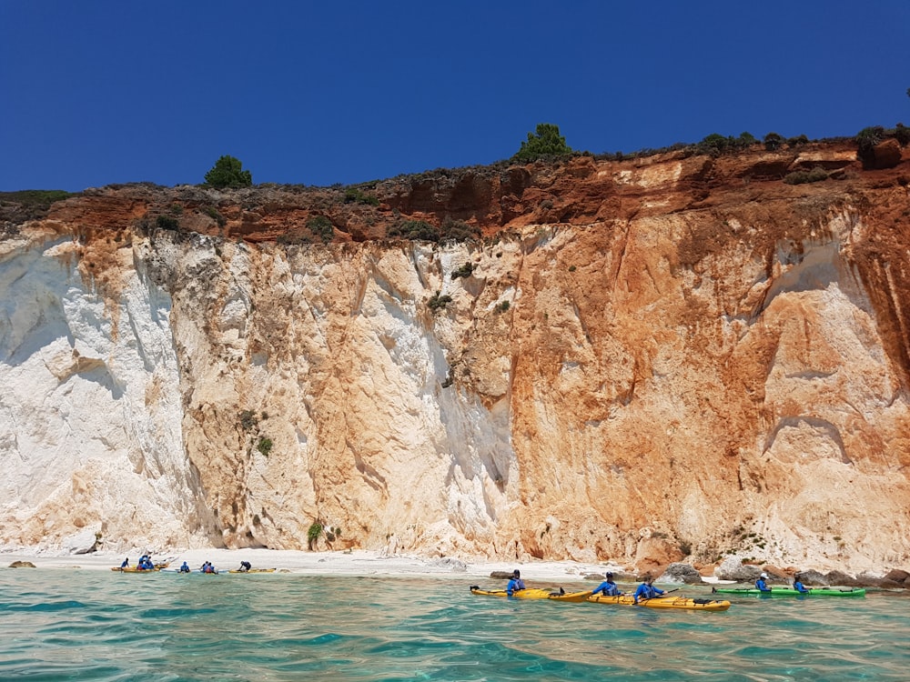 people riding on yellow kayak on blue sea near brown rock mountain during daytime