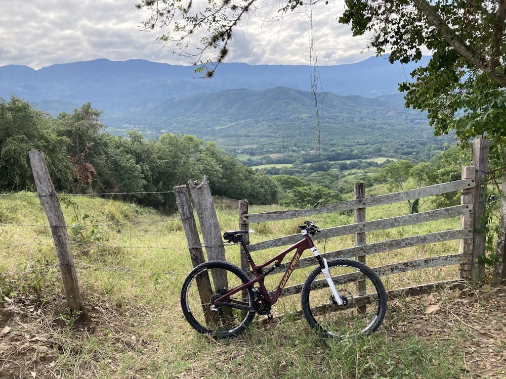 Bicicleta de montaña negra y roja en valla de madera marrón durante el día