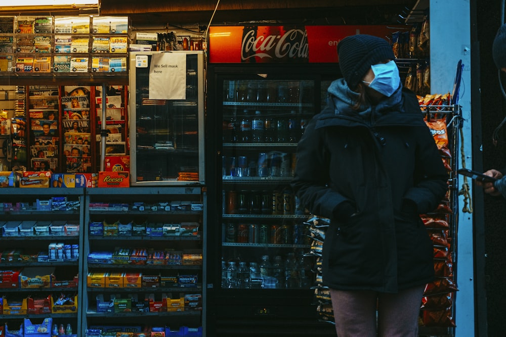 man in black jacket standing near coca cola vending machine