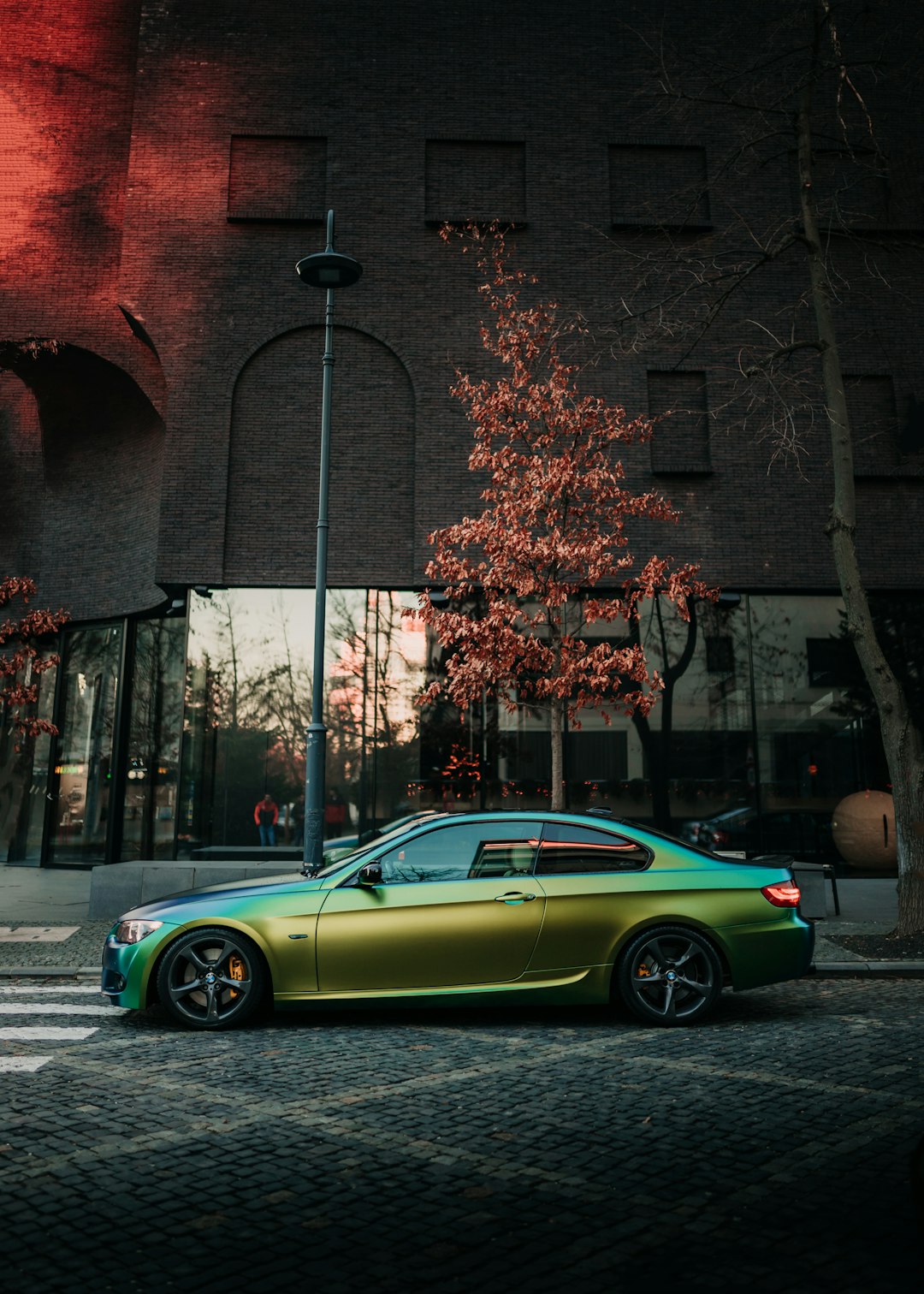 green coupe parked beside brown brick building during daytime