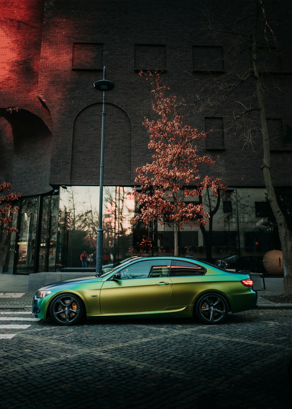 green coupe parked beside brown brick building during daytime