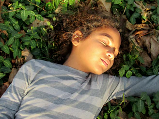 A calm moment of a child gently exploring leaves in a sunlit garden.