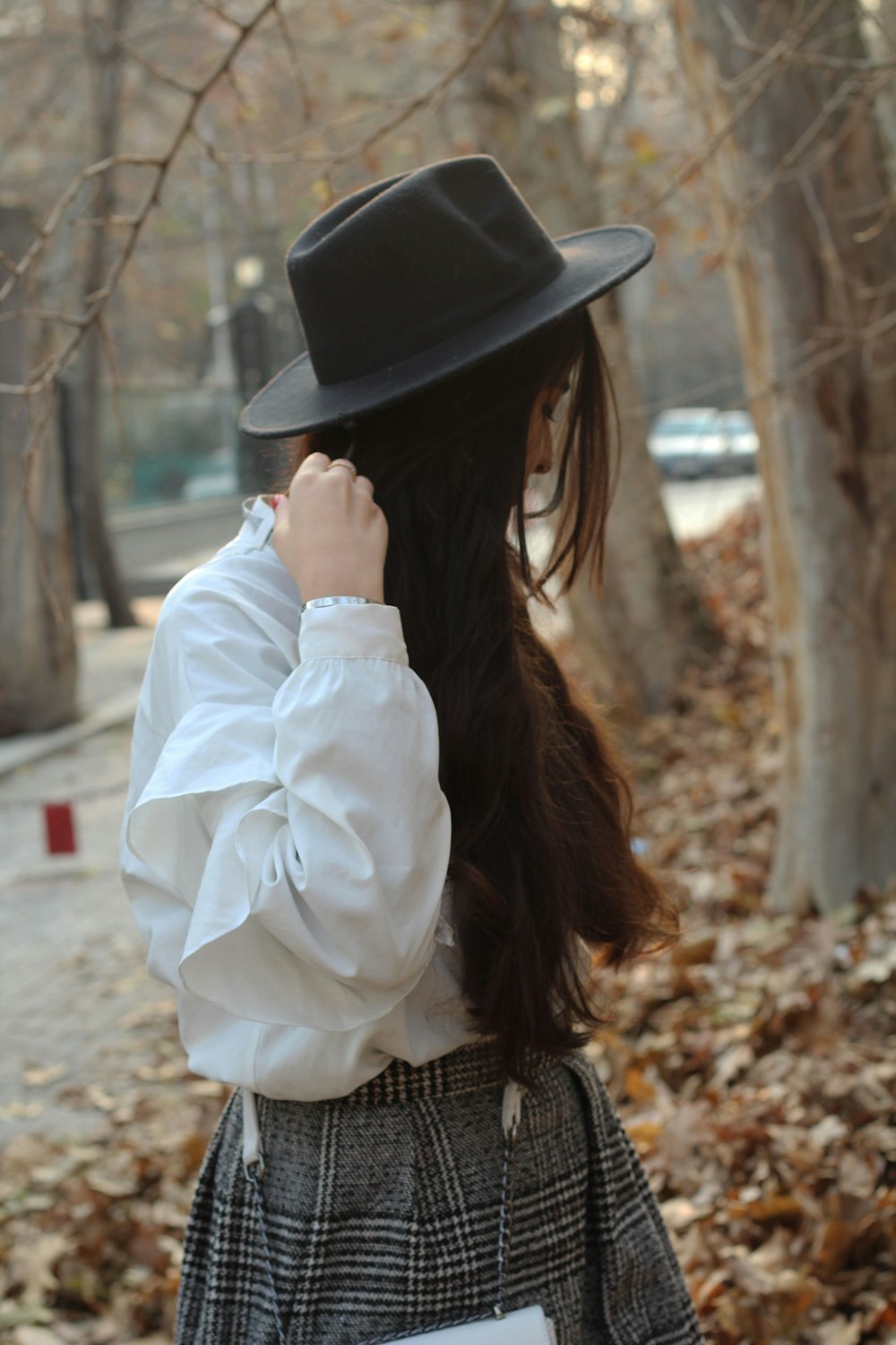 woman in black and white checked shirt wearing black fedora hat standing near brown tree during