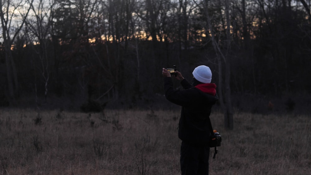 man in black jacket holding camera taking photo of trees during daytime