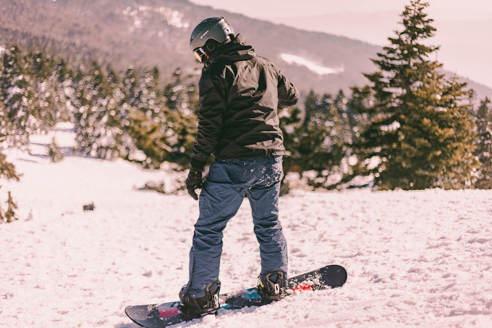 Mann in schwarzer Jacke und blauer Hose, der tagsüber auf schneebedecktem Boden steht